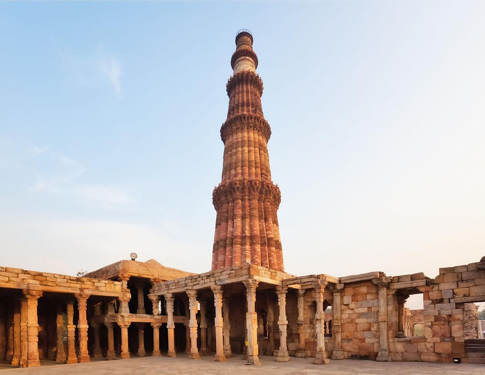 Tall red sandstone minaret rising over ancient stone ruins and arches under a clear blue sky, calm historic scene. India Sightseeing Tour