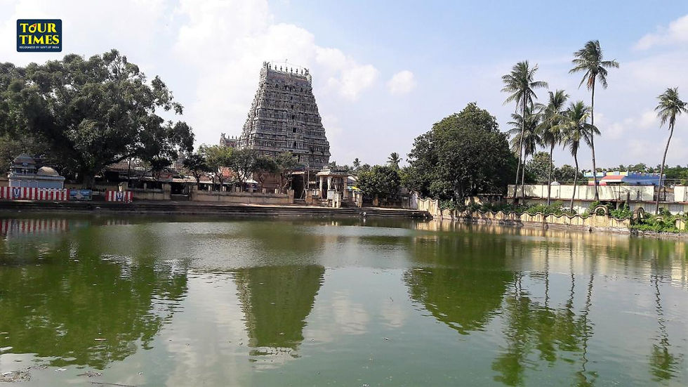 Ancient temple with a towering gopuram beside a serene green pond and trees under a cloudy sky. "TOUR TIMES" logo at the top left.