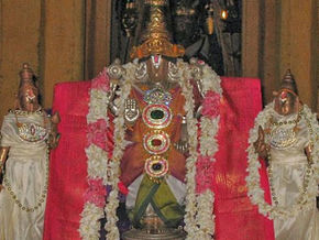 Decorated Hindu temple idols with garlands and jewels, central deity flanked by two figures before a red backdrop; Tour Times watermark.Thirukulandhai Temple