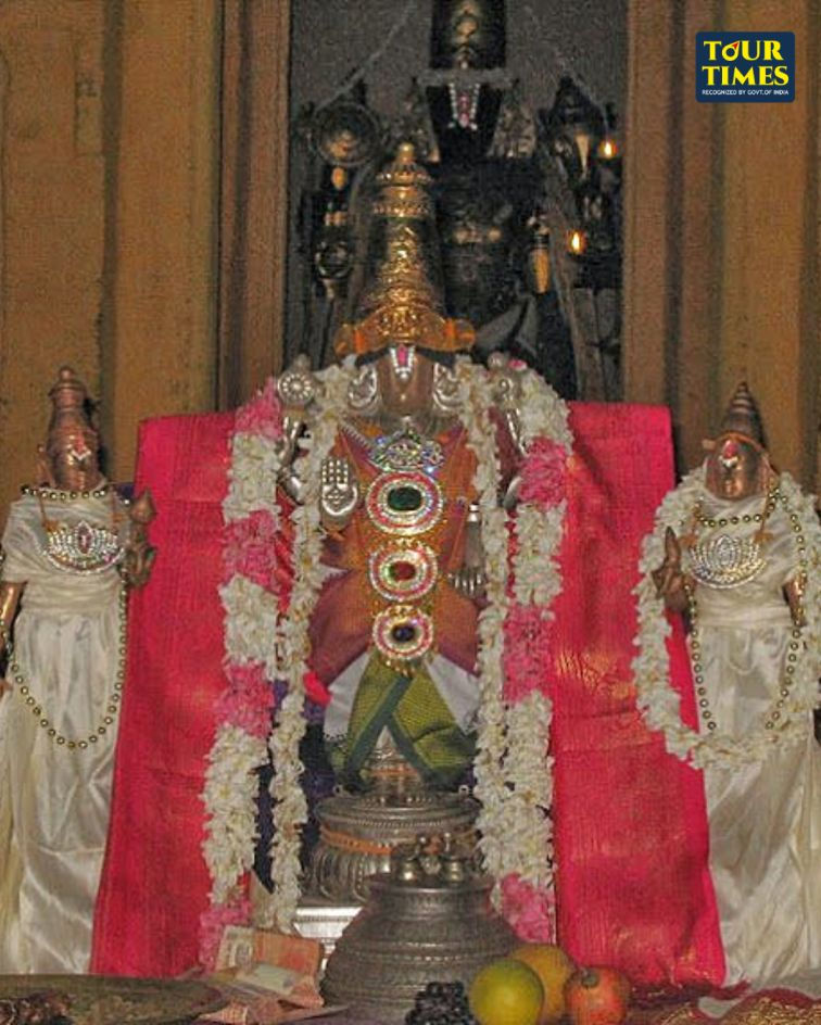 Decorated Hindu temple idols with garlands and jewels, central deity flanked by two figures before a red backdrop; Tour Times watermark.Thirukulandhai Temple