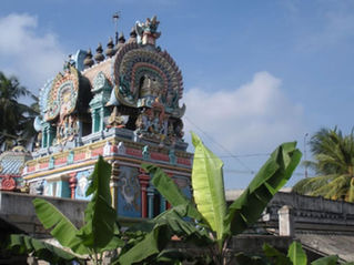 Colorful Hindu temple tower with ornate carvings, framed by palm trees and banana leaves under a blue sky; Tour Times logo.hirukkarambanoor Temple