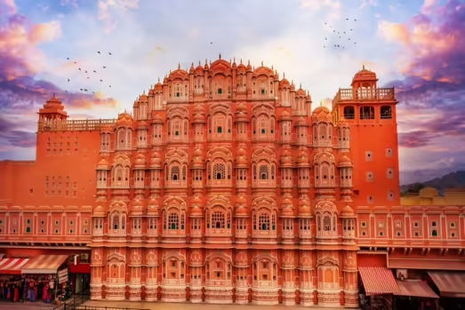 Pink Hawa Mahal palace in Jaipur under a colorful sunset sky with birds flying overhead. India Sightseeing Tour