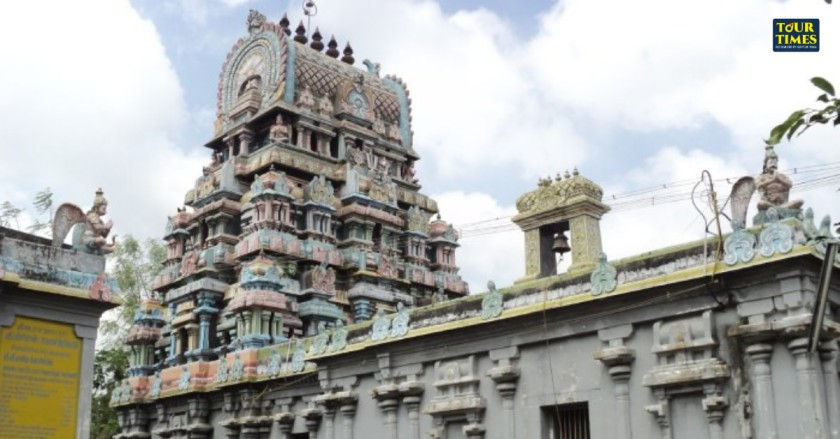 Ornate temple with colorful carvings under a partly cloudy sky. Yellow plaque visible on the side wall. Mood is serene. Tour Times logo.Thiruthetriyambalam Temple