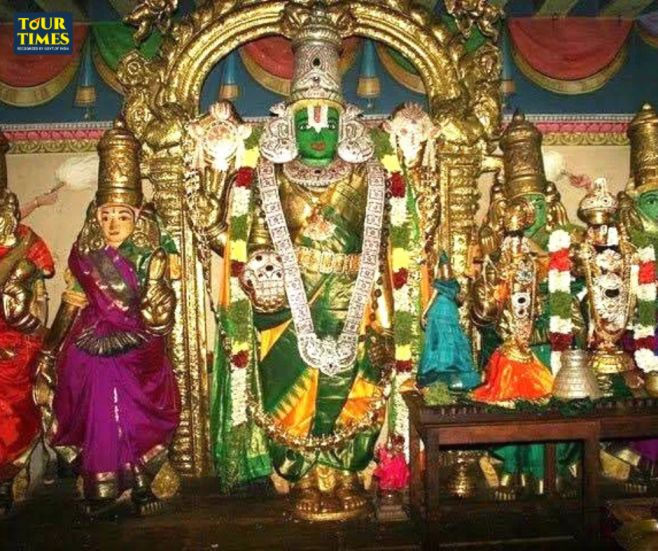 Colorful Hindu temple idols, centered on a green-faced deity in a gold arch, with smaller statues and a TOUR TIMES watermark. Thirutholaivillimangalam Temple