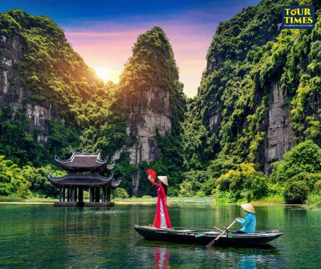 Woman in red áo dài waves from a boat on a calm river; rower in conical hat, karst cliffs, pavilion, sunset, Tour Times logo. Tourist Spot in Cambodia and Vietnam
