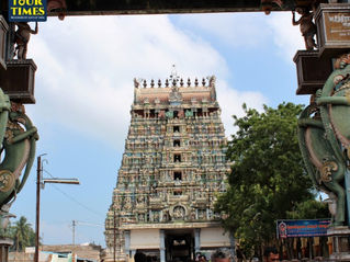 Crowd enters a colorful Hindu temple gopuram framed by carved gate pillars under a blue sky, with TOUR TIMES watermark.