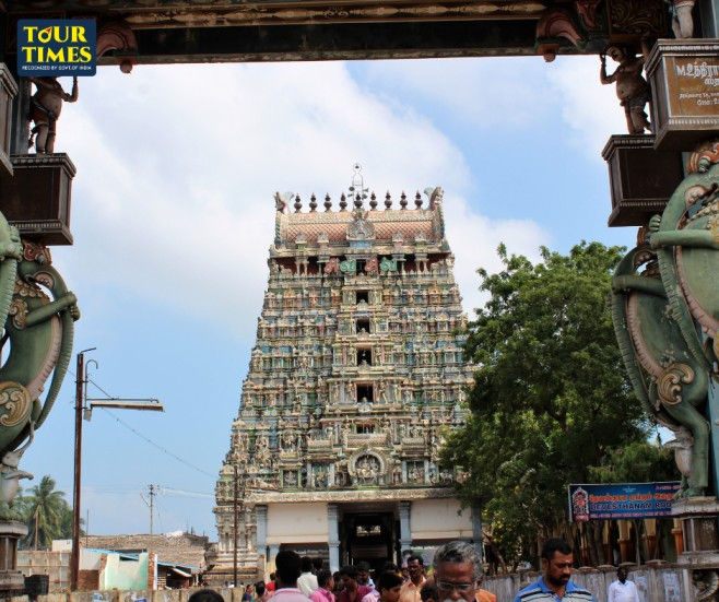 Crowd enters a colorful Hindu temple gopuram framed by carved gate pillars under a blue sky, with TOUR TIMES watermark.