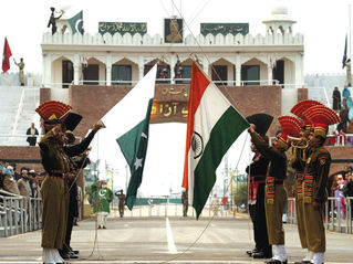 Border ceremony with Pakistani and Indian soldiers facing off, flags raised before a grand gate at the Wagah border.