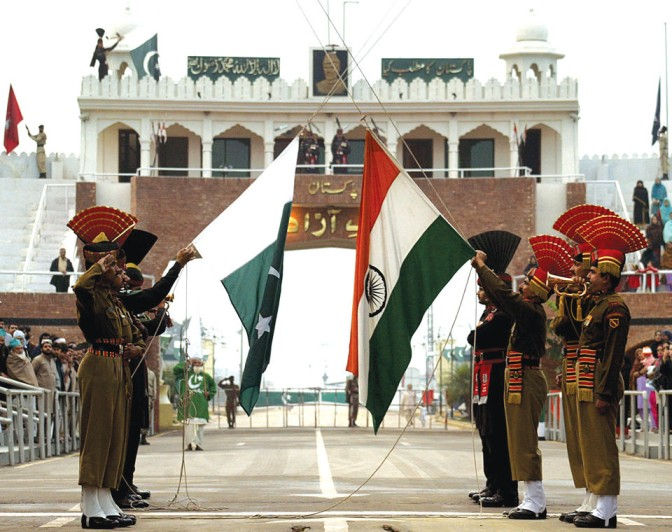 Border ceremony with Pakistani and Indian soldiers facing off, flags raised before a grand gate at the Wagah border.