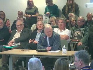 A member of the public sitting at desk speaking with microphone at full council meeting