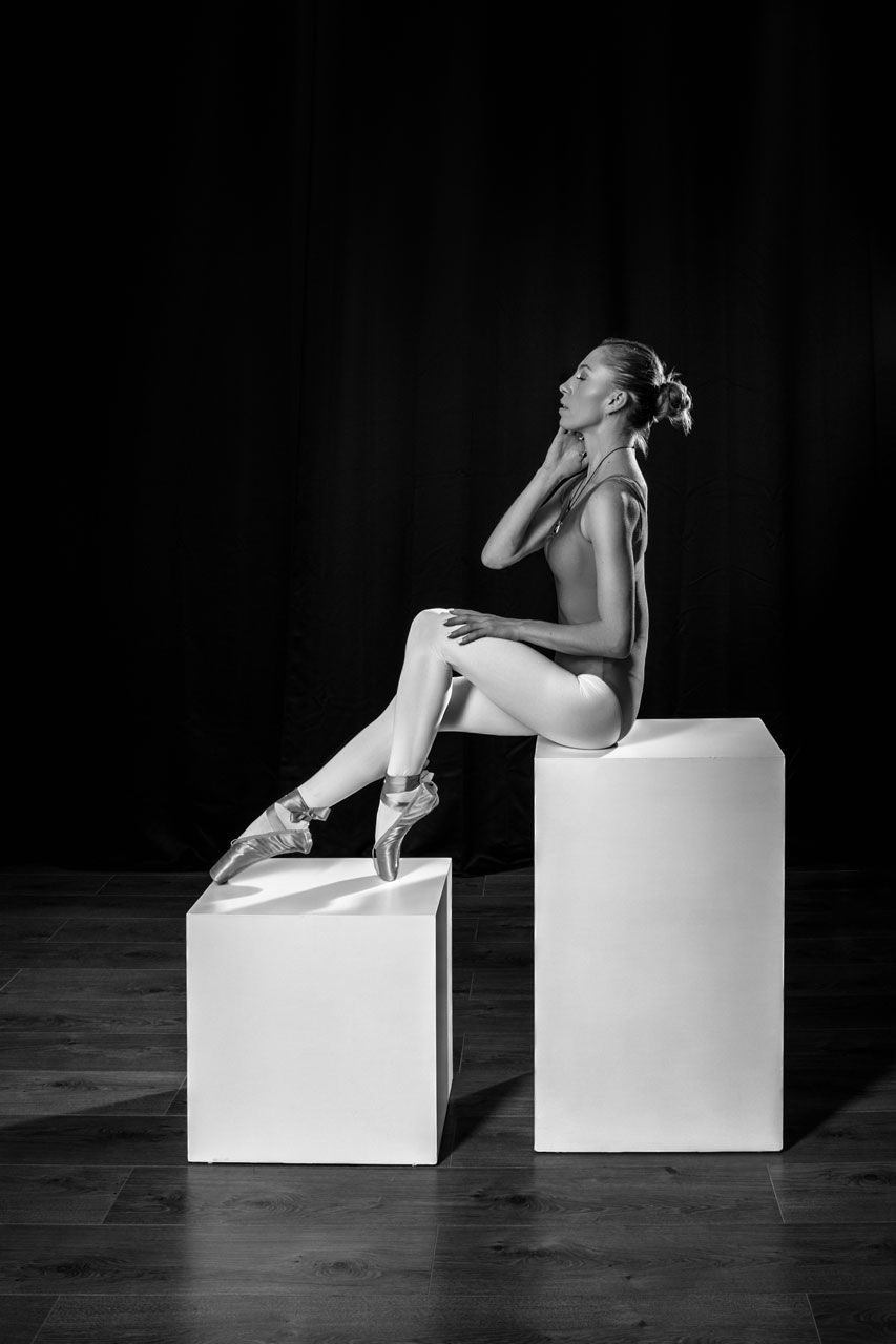 Black and white portrait of a ballerina sitting on posing boxes in the studio.