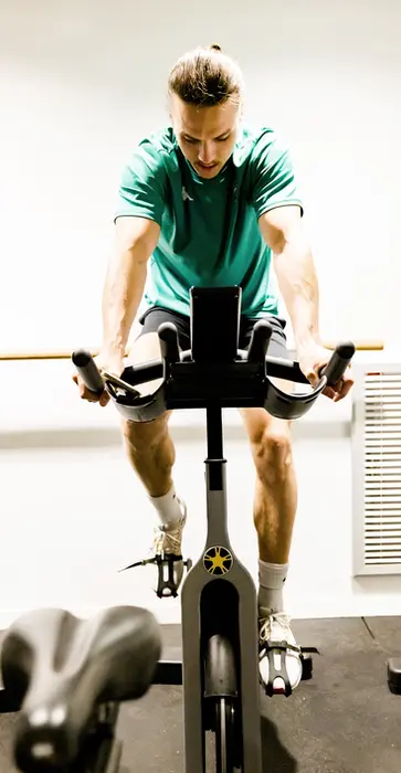 Athlète concentré sur un vélo de training en salle, illustrant le travail d’endurance et de vitesse au sein des méthodes Powerforge axées sur la performance répétée