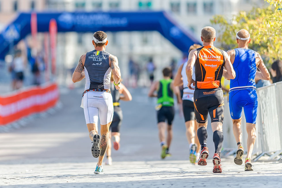 Runners in colorful gear participate in a race on a sunny day, with a blue finish line banner in the background and cheering spectators.