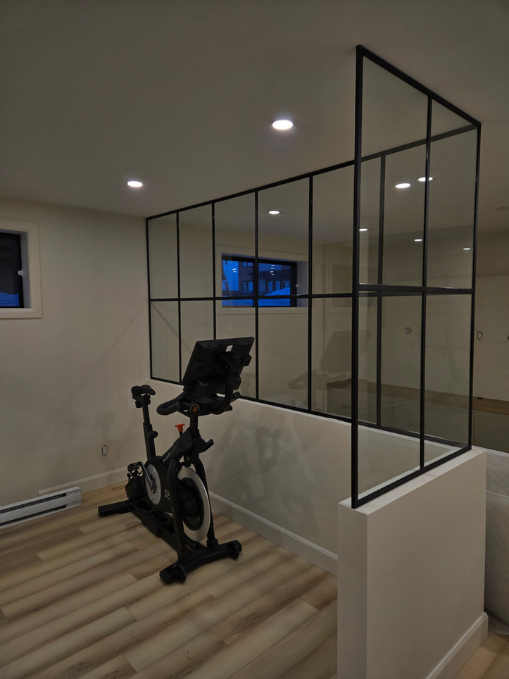 Coin gym dans un sous-sol avec demi-mur combiné à des panneaux vitrés sur cadre en métal pour mieux diviser l'occupation de l'espace sans compromettre la luminosité.