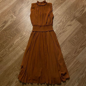 A burnt orange, mock neck, tea-length dress with pleating and a smocked waistband.