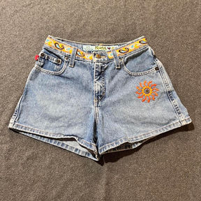 Light wash denim shorts with an embroidered sunflower on the left hip and paisley trip along the waistline.