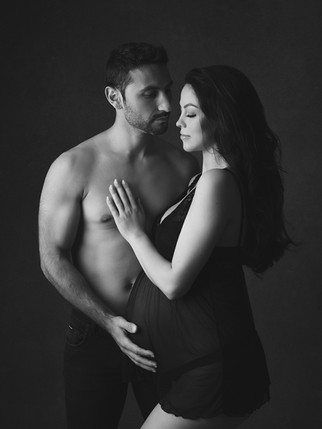 Um casal em uma sessão fotográfica de grávida. O marido está sem camisa, com a mão na barriga da mulher grávida