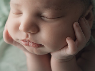 Close de perfil do rosto de um bebé. Ele está com os olhos fechados e com o rosto apoiado nas mãos