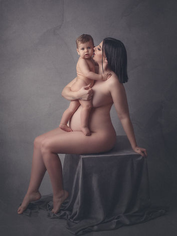 Mulher grávida em sessão fotográfica de nú artístico , com filho nos braços. Ela dá um beijo e ele olha para a câmara.