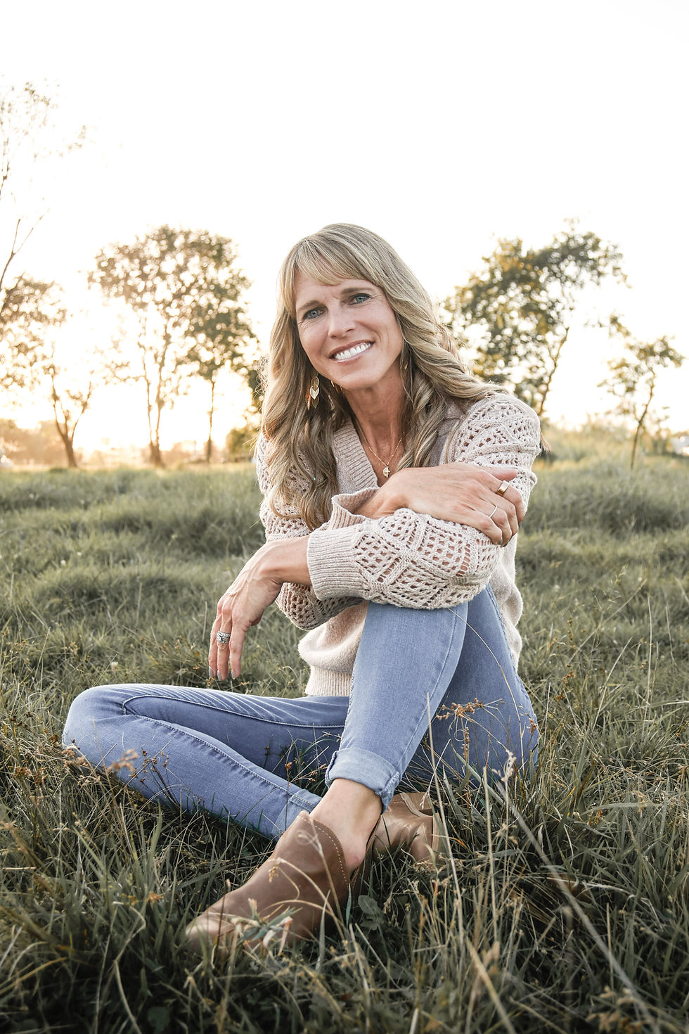 Jessica Tritz, founder of Central Wisconsin Bernedoodles, sitting in a grassy Wisconsin field at sunset.