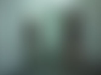 A woman facing a mirror in a softly lit, minimalist room. She’s barefoot, standing in reflection, with one hand resting gently on the mirror. Her expression is contemplative but grounded. The mood is raw, calm, and powerful.