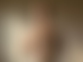 A woman standing alone in a softly lit room with one hand over her heart and the other on her abdomen, eyes closed, exhaling deeply. Her posture is grounded, not posed. Neutral tones, warm shadows.