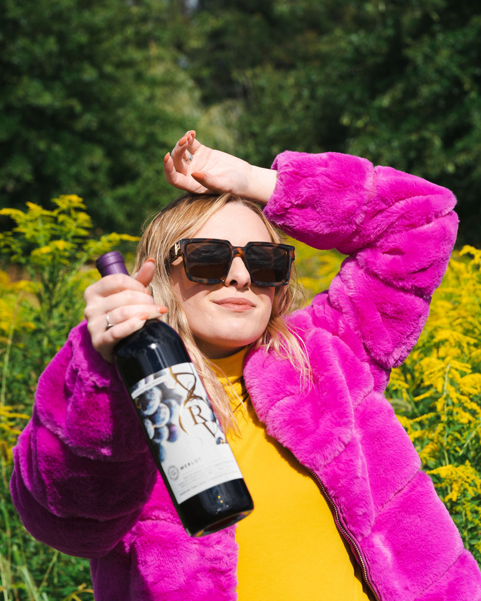 Girl in bright pink coat holding a bottle of Running Vines Merlot