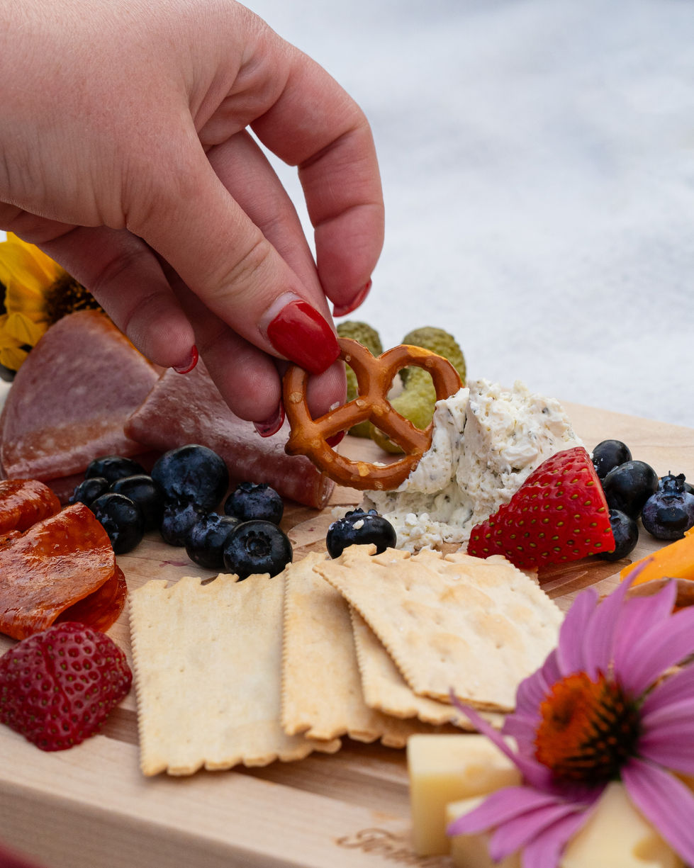 Hand grasping a pretzel that is being dipped into a spread located on a charcuterie tray