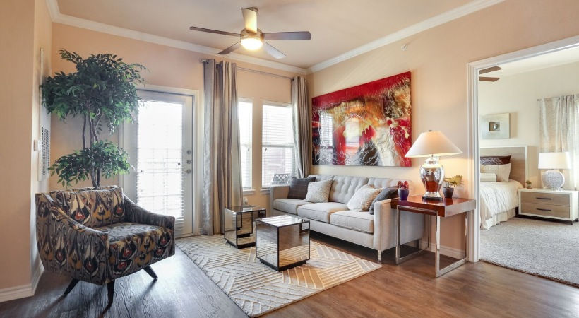 Living room of apartment model with mid-century modern sofa, tufted back pillows, mirrored cube tables, garnet and gold epoxy art piece, and ikat chair.