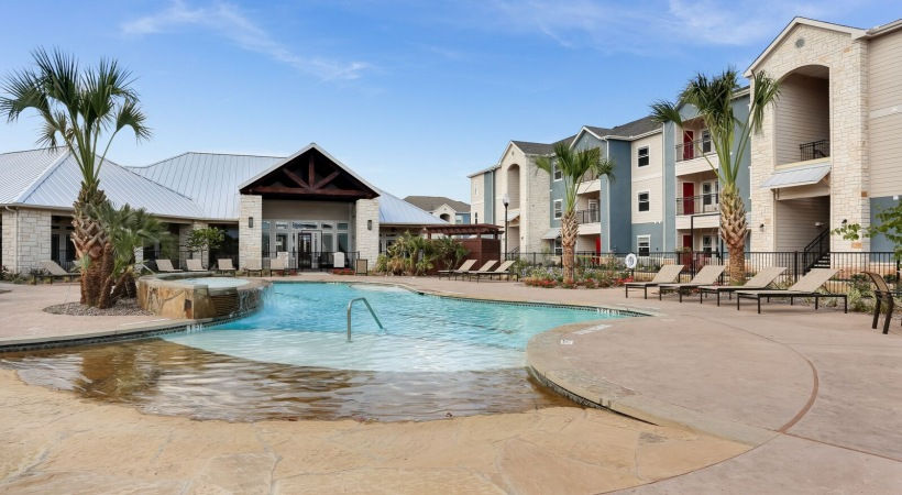 Apartment pool at Residences at Midland with the clubhouse in the background, featuring lush landscaping and tranquil waters.