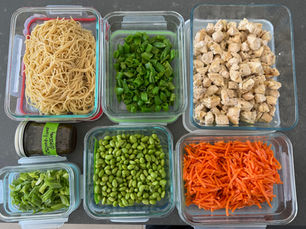 Components for sesame chicken noodle salad: noodles, sliced snap peas, diced chicken, edamame, shredded carrots, scallions and a jar of sesame-lime dressing in separate glass containers