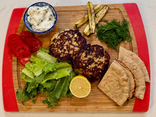 Components for Greek turkey and feta burgers: seared patties, sliced vegetables, feta, and tzatziki