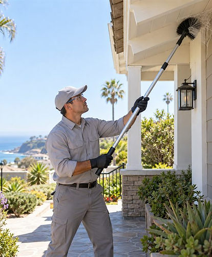 Pest control technician using an extendable brush to remove spider webs from a home's exterior porch eaves during pest control services in Marin County, CA