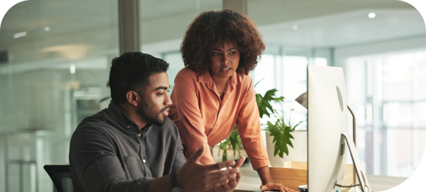 Two professionals collaborating at a desk, discussing business strategy while reviewing information on a computer screen.