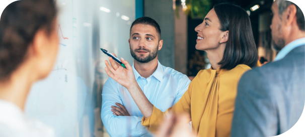 Business team in a meeting, woman presenting data on a whiteboard while colleagues listen and discuss strategies