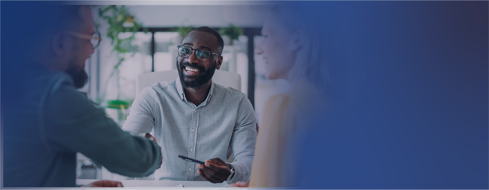 Smiling financial advisor shaking hands with a client during a meeting, with another person at the table.
