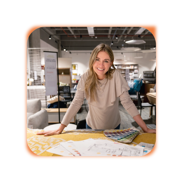 Smiling interior designer leaning over a table with fabric samples and design plans in a furniture showroom