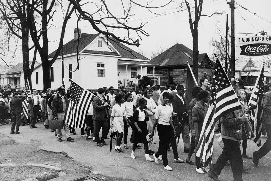 Black people marching with flags from selma to montgomery, AL, pushing for the voting rights act of 1965.