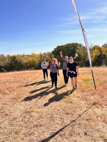 Group of women walking, waving, clear skies background, outdoor event, cheerful moment.