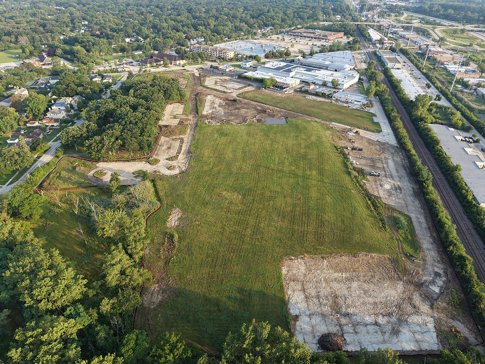 Aerial construction site photo, wide landscape, showing graded land and surrounding trees and buildings