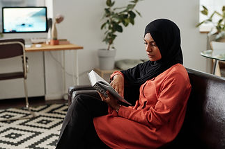 Young Muslim female student in hijab and casualwear reading psychology encyclopaedia while revising home assignment or preparing for exam.jpg