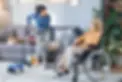 Haushaltshilfe saugt Staub und unterhält sich mit einer Seniorin im Rollstuhl