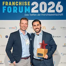 Okan Elibol, Geschäftsführer der Eli die Fee Franchise GmbH freut sich gemeinsam mit Lukasz Mehl, der in diesem Jahr der unabhängigen Jury angehörte, über den gewonnen Award zum Franchisesystem des Jahres 2026.
