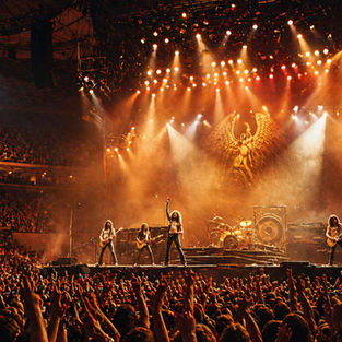 1970s arena rock concert with a massive crowd, band performing on a large stage with bright lights and high-energy atmosphere