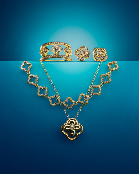 A gold clover-themed jewelry set, including a necklace, bracelet, ring, and earrings, elegantly displayed against a blue gradient background.