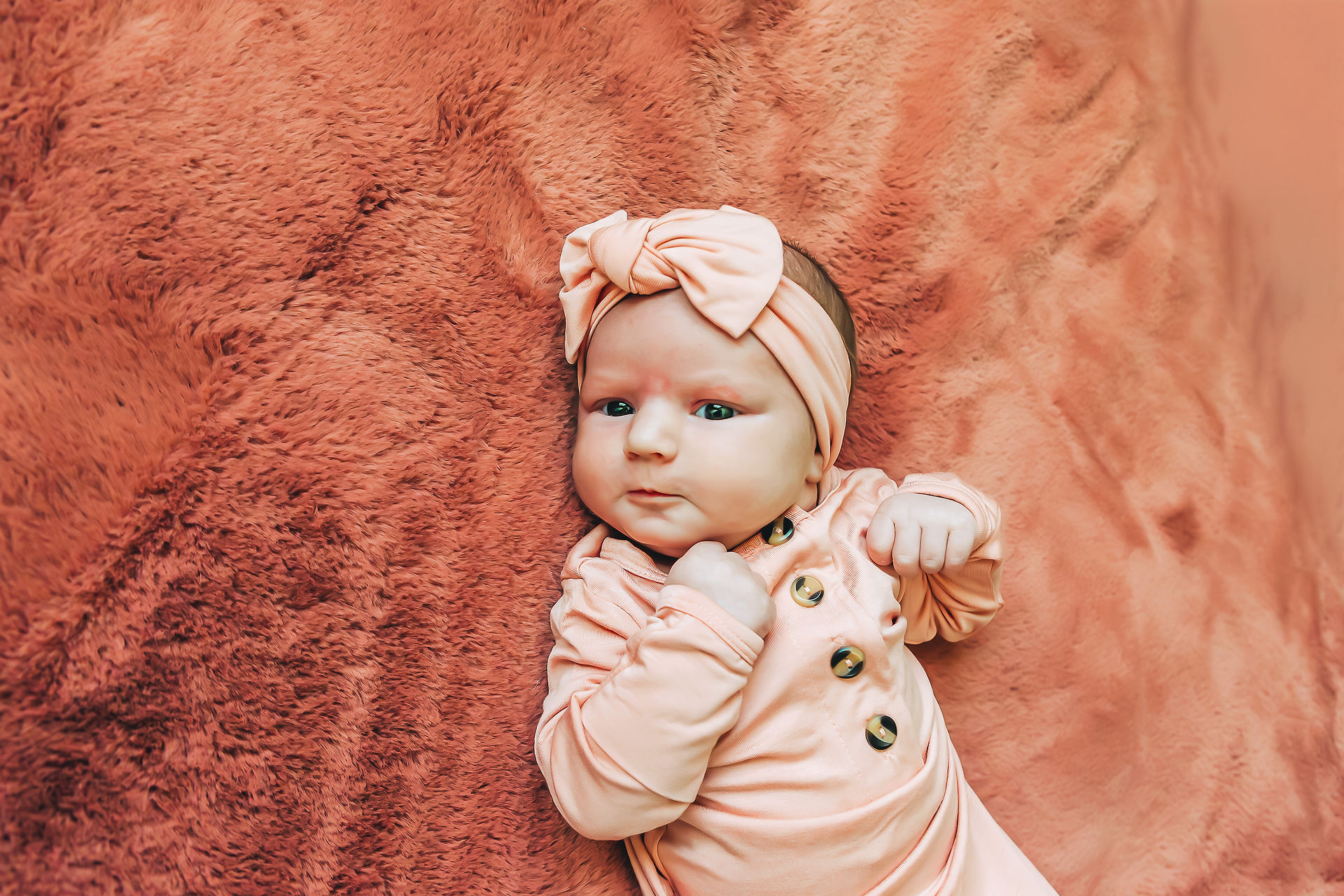 newborn baby girl wearing pink bow and laying on pink fluffy rug