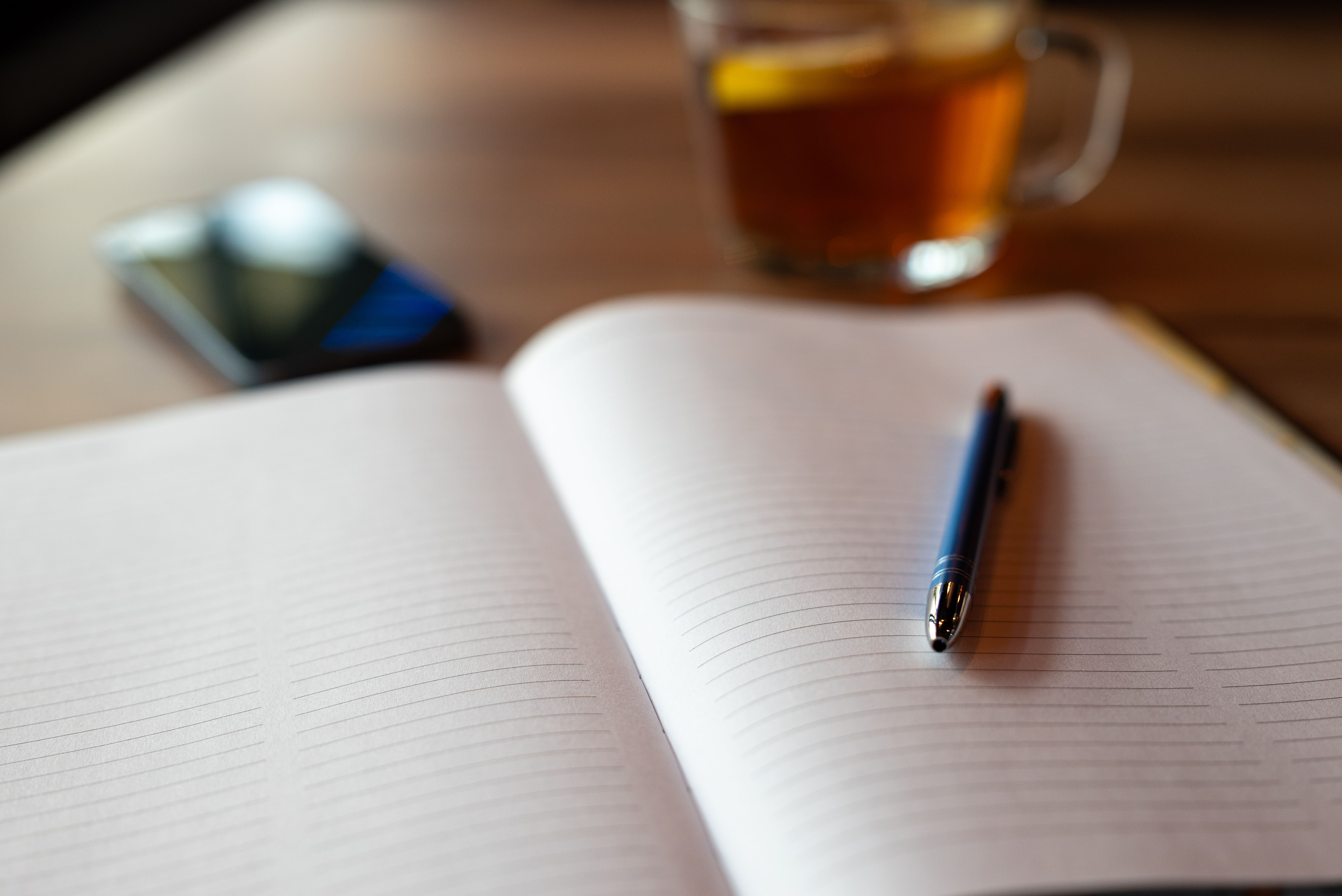 An open notebook with a pen, smartphone and tea on a wooden table