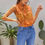 Thumbnail: Model wearing Radiant Sun - Women's Sleeveless Top in bright orange with white specks and built in neck tie