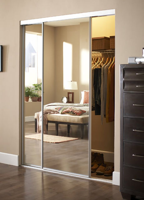 Mirrored sliding closet doors reflecting a bedroom with a bed, dresser, and clothes hanging