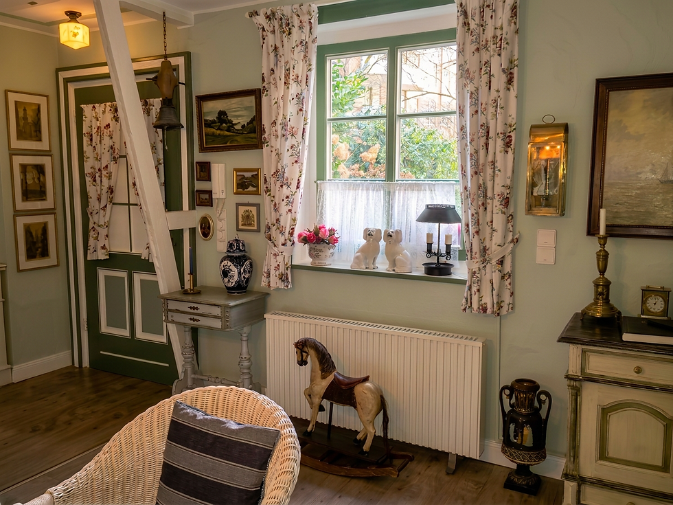 Interior photography of a cozy, rustic cottage living area. The room features soft green walls, floral curtains, a wooden rocking horse, and traditional country-style decor.